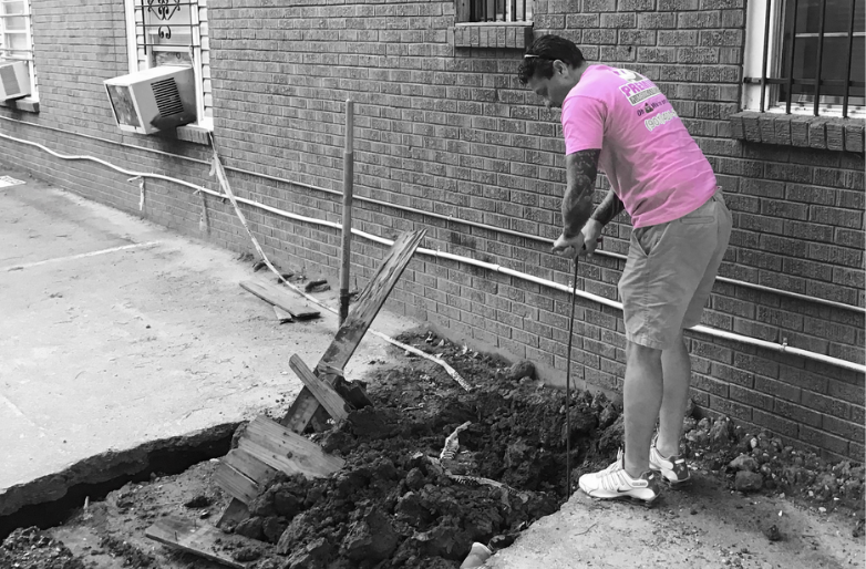 Premier plumber in a pink shirt digging out a sewer line beside a Memphis home